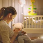 Young beautiful mother, breastfeeding her newborn baby boy at night, dim light